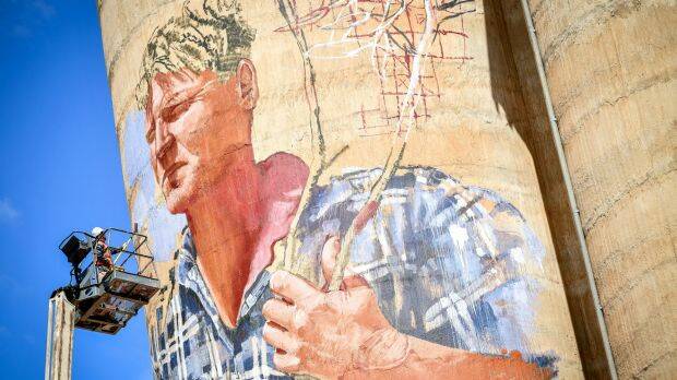 Artist Fintan Magee, in cherry-picker, works on the silo mural of farmer in Patchewollock.