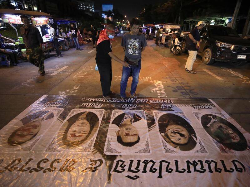 Protesters studying posters, including one of the Thai PM who has ignored demands to resign.